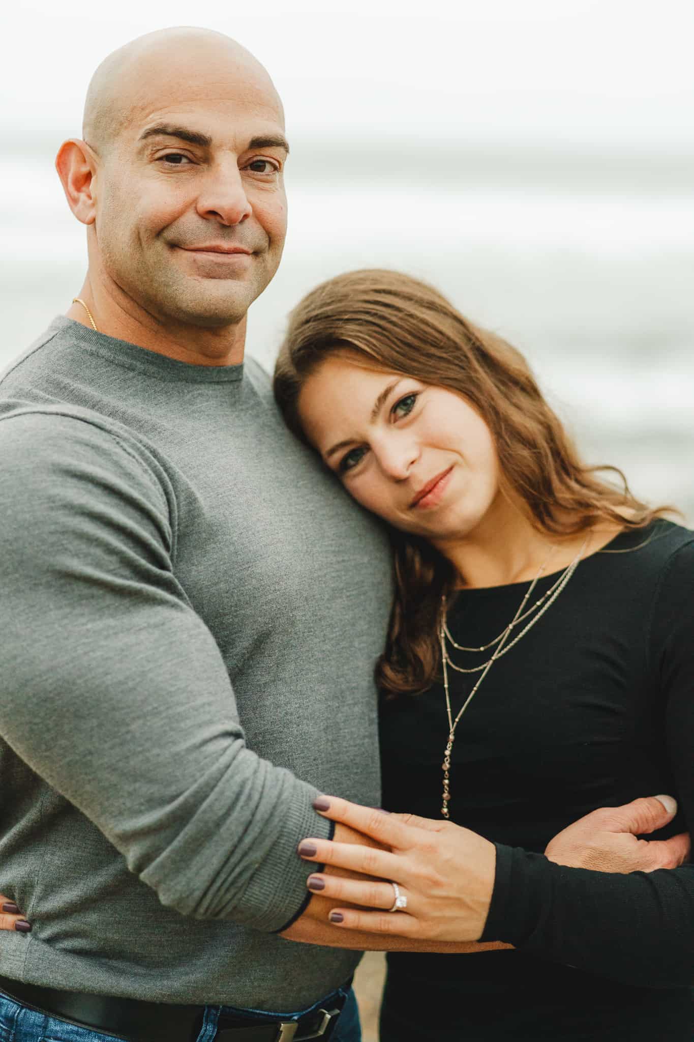 Beach portrait of a couple during their engagement session at the Montauk lighthouse in Long Island New York with Gray water background