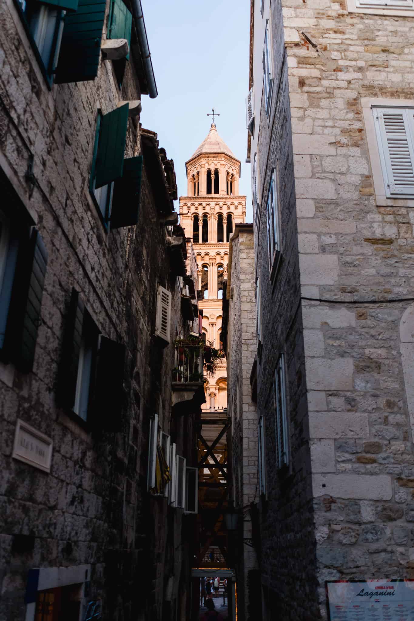 A photo of the Saint Dominus bell tower lit up by the sun with dark buildings in the foreground in the city of split Croatia