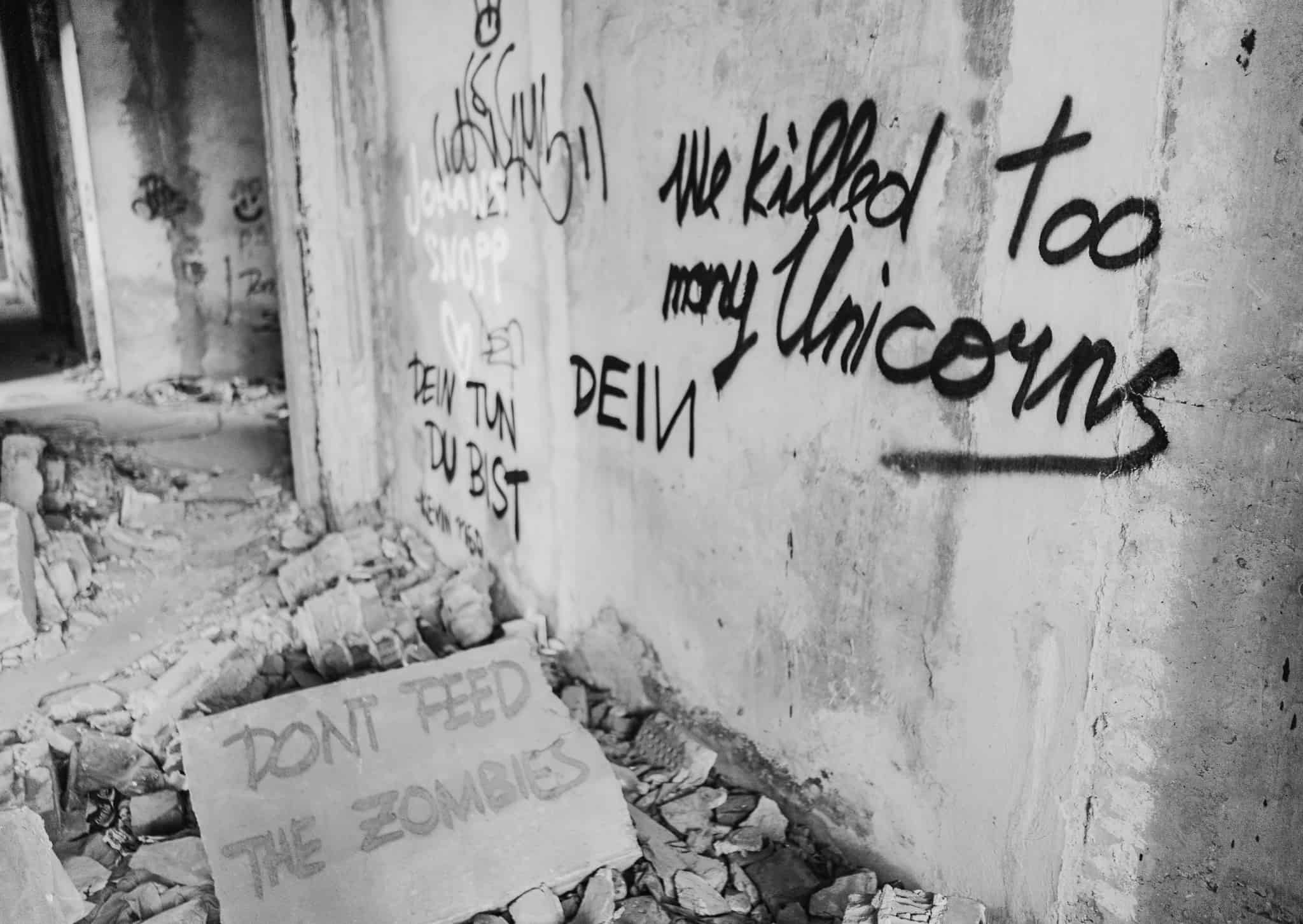 Black and white photo of graffiti in the Mostar sniper tower in Bosnia and Herzegovina that reads "we killed too many unicorns" and "don't feed the zombies"