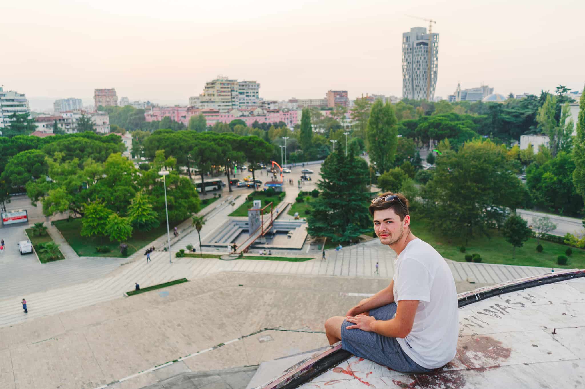 Tristan Wallace sitting on top of the rundown pyramid of Tirana in Albania with the city in the background at sunset
