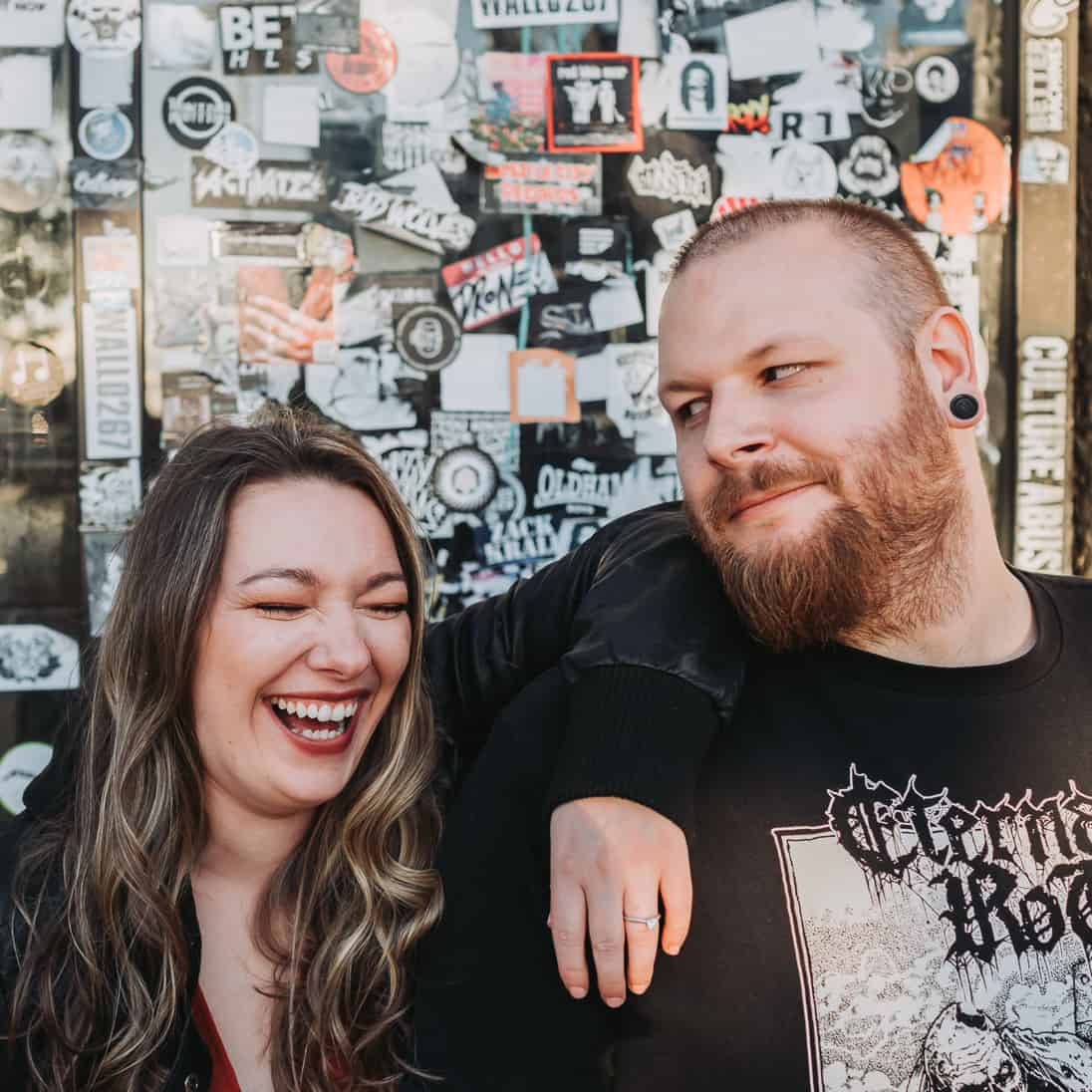 Cute couple laughing with each other during their engagement session and fishtown Philadelphia in front of rock venue and band stickers