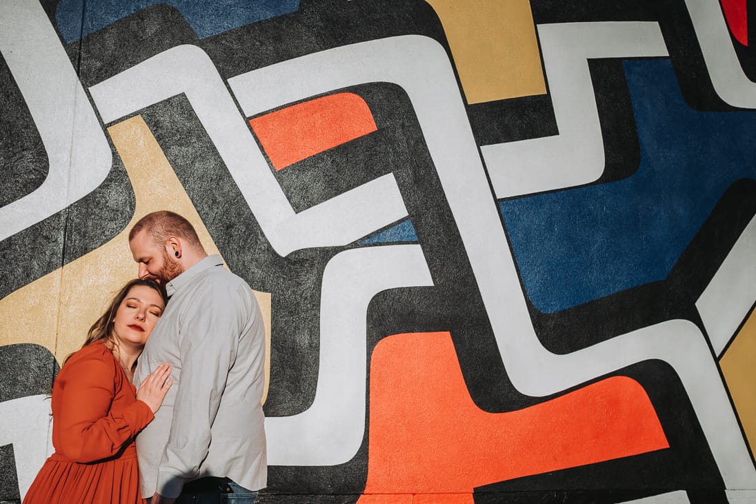 Super cute couple hugging with their eyes closed in front of pop art graffiti in fishtown Philadelphia for their engagement photoshoot