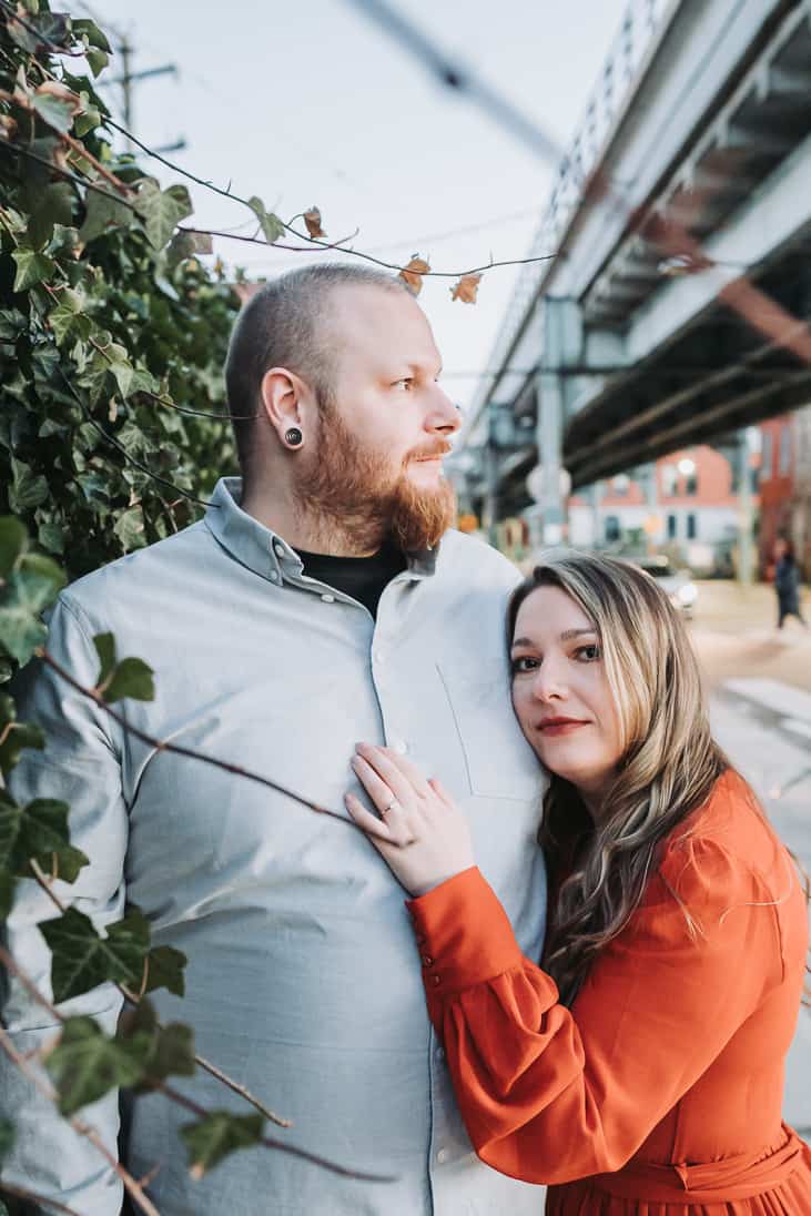 Engagement photo of a couple leaning together on an Ivy Bush near the SEPTA and fishtown Philadelphia during sunset