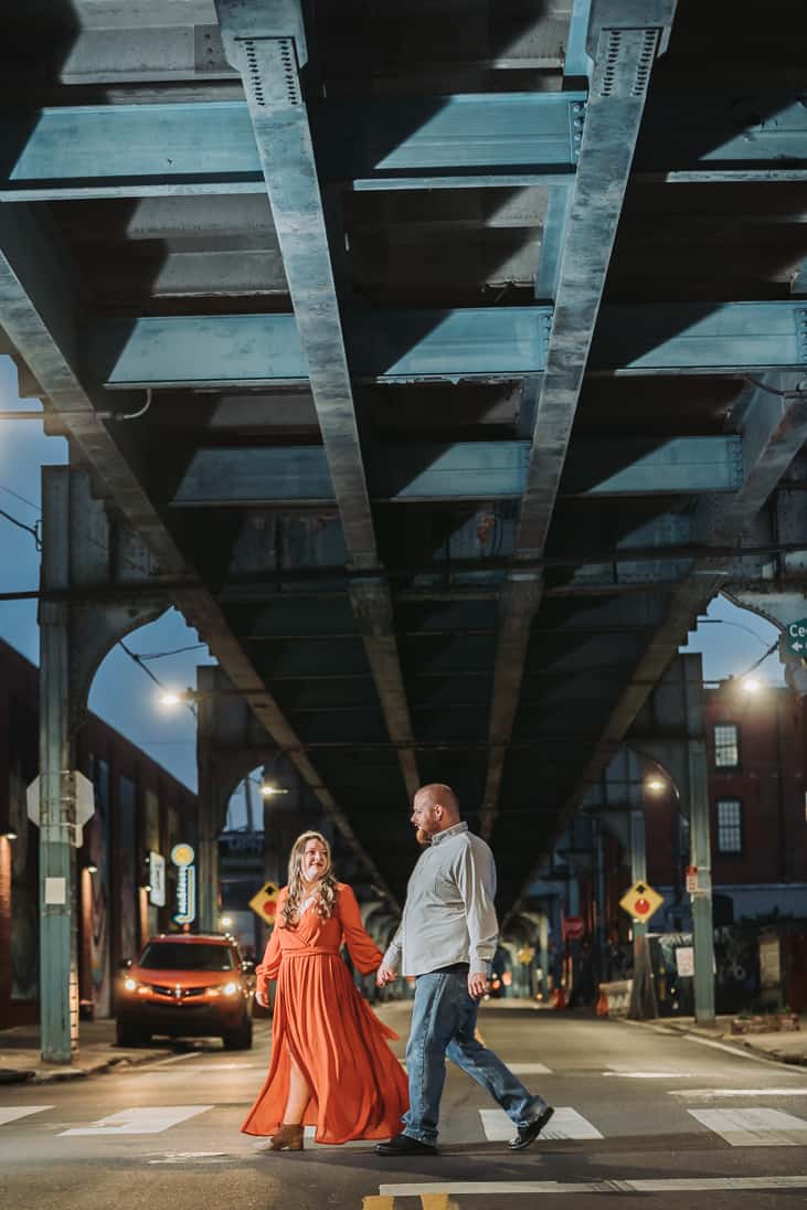 Engagement photo of a couple walking under the SEPTA in fishtown Philly dramatically lit