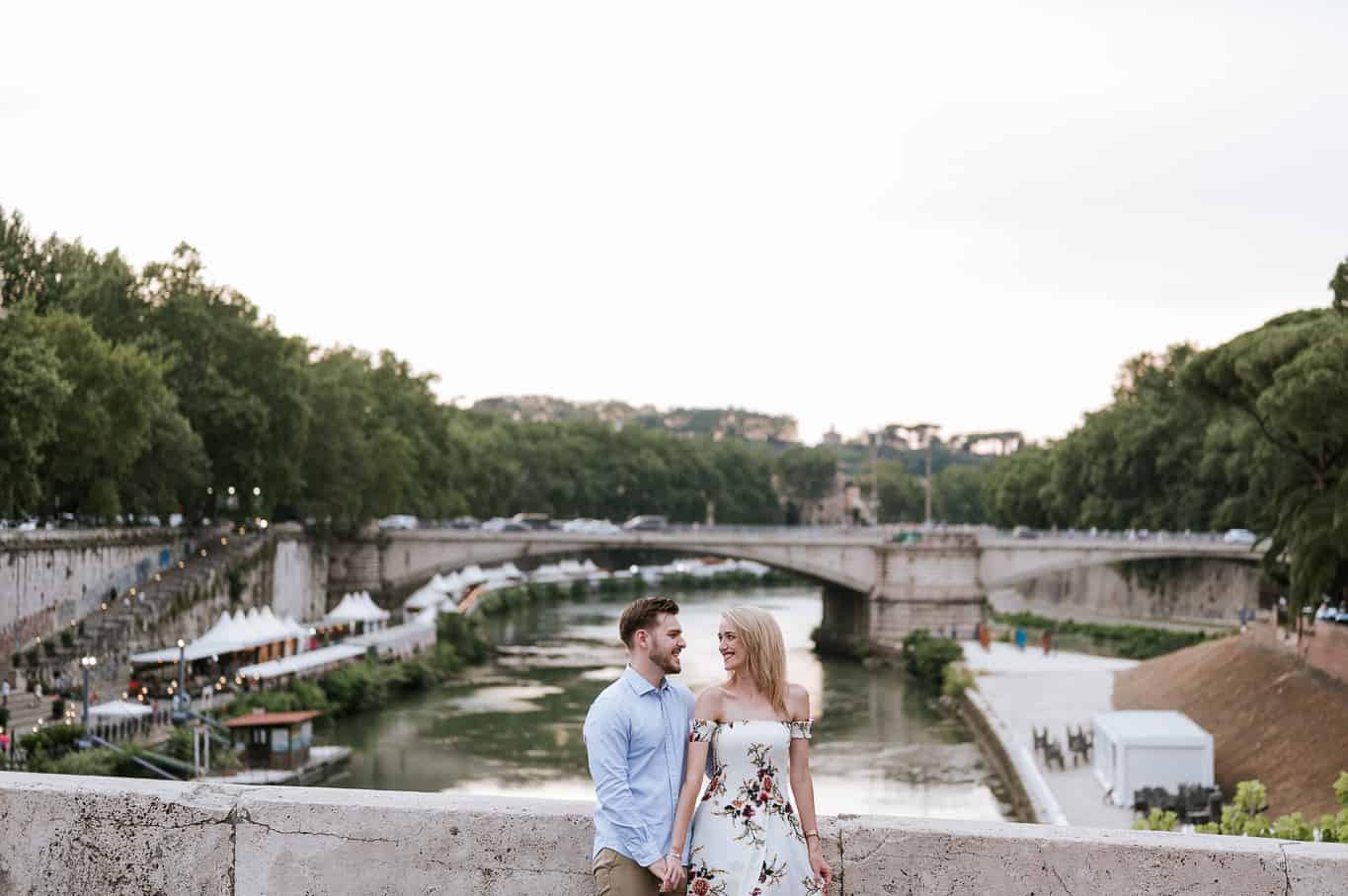wide epic photo of couple laughing during engagement photo shoot in front of the tiber river during sunset in Rome Italy