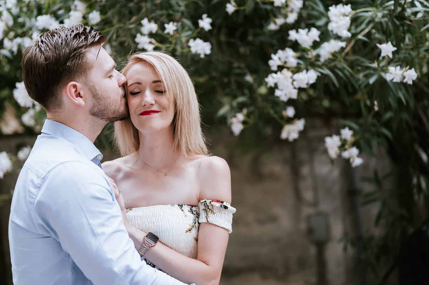 couple nuzzling with eyes closed during engagement photo shoot in front of greenery and white flowers on streets of Rome Italy  