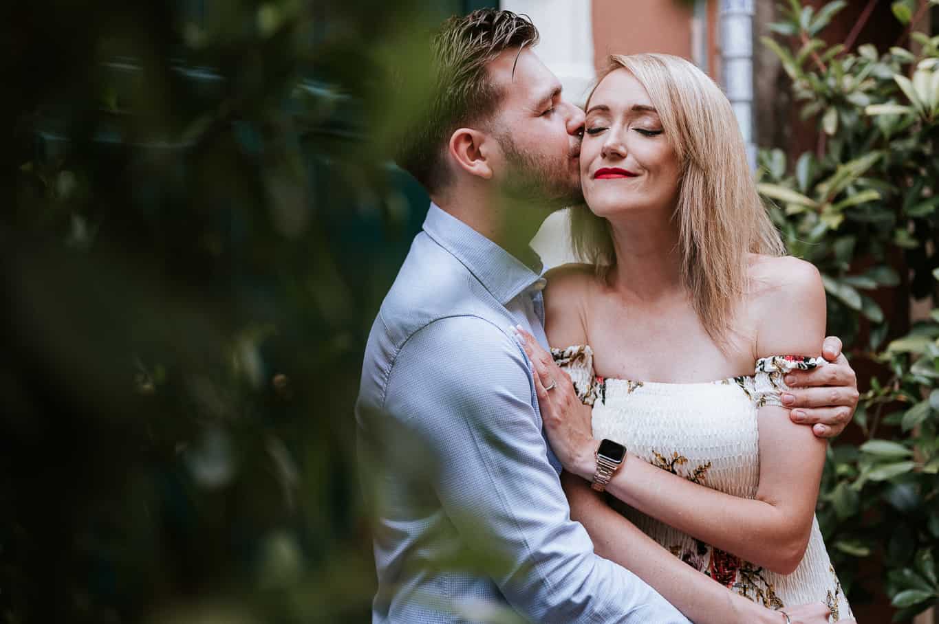 Couple snuggling during engagement photo shoot in front of Bushes on the streets of trastever in Rome Italy