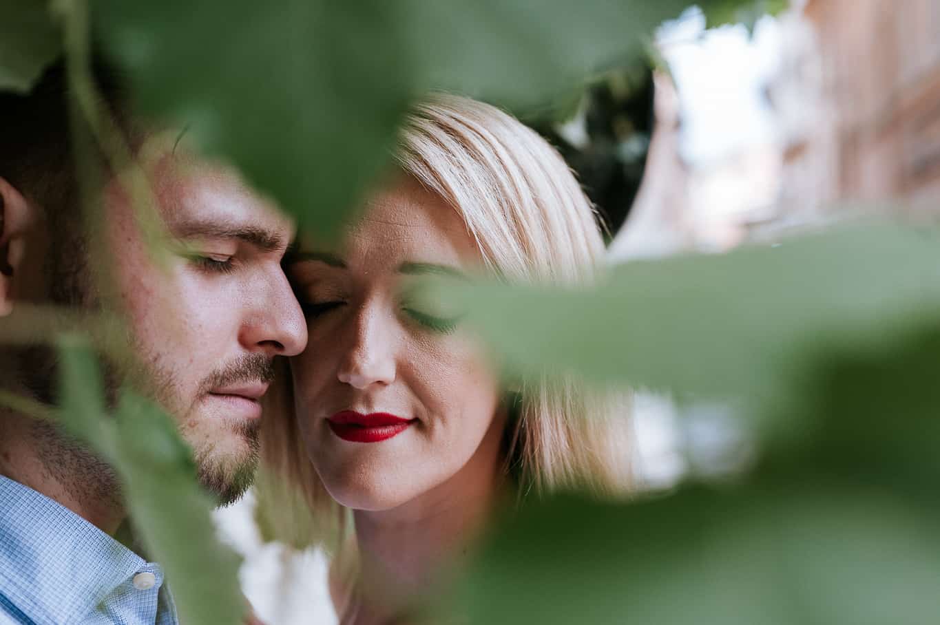 close up photo of couple with eyes closed during engagement photo shoot on the streets of trastevere in Rome Italy with large leaves in the foreground