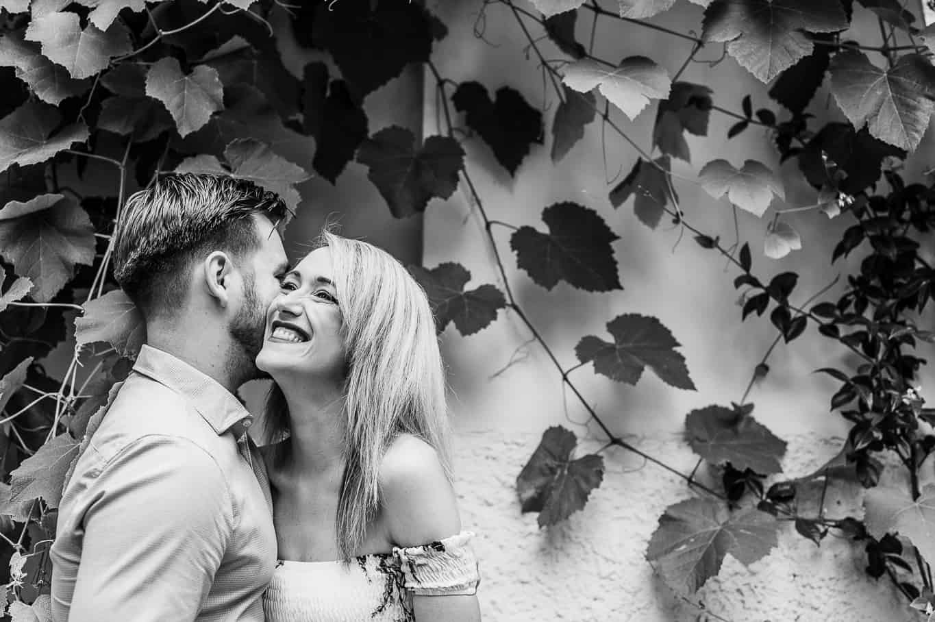 Black and white photo of couple laughing during engagement photo shoot in front of Ivy covered walls on the streets of trastevere in Rome Italy
