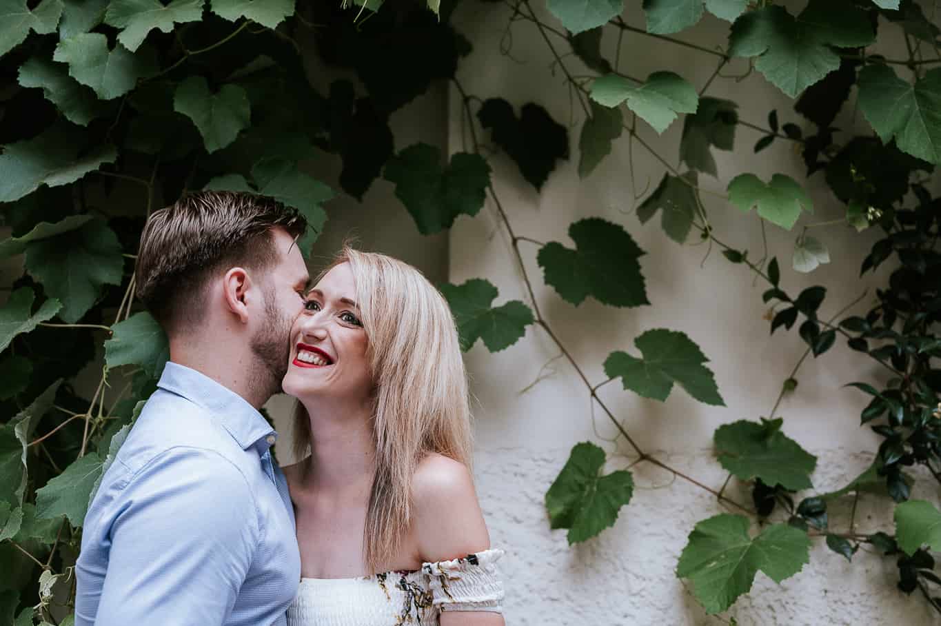 Couple laughing during engagement photo shoot in front of Ivy covered wall on the streets of pressed every in Rome Italy